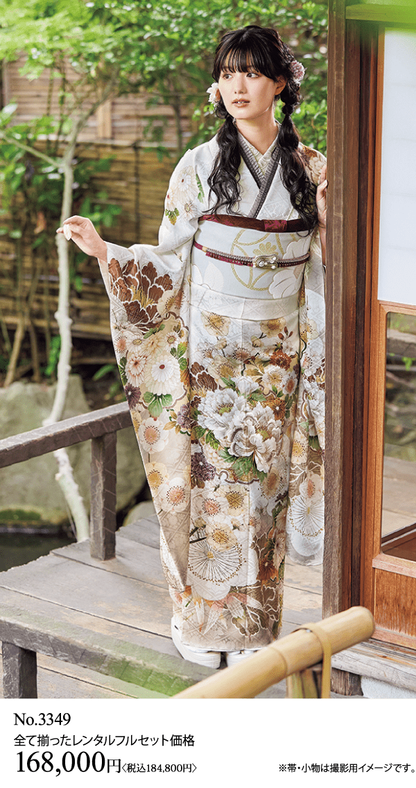 花柄の着物を着た女性が、木造の建物と緑の近くの外に立っています。.
