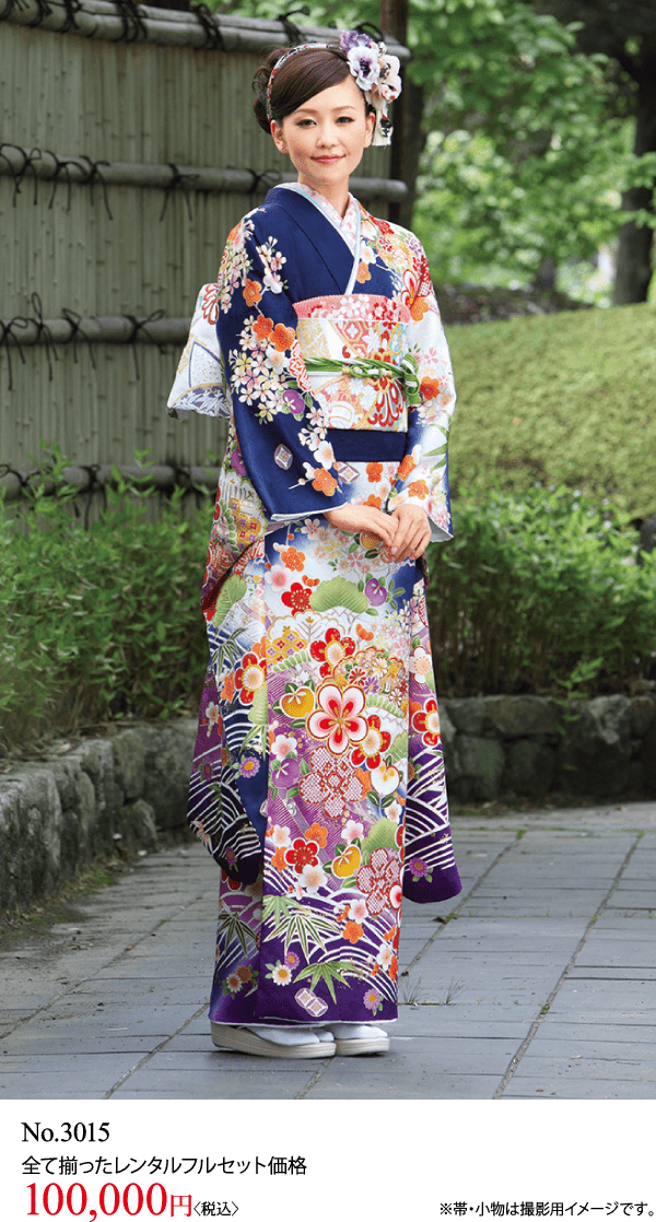 色鮮やかな花柄の着物を着た女性が、緑を背景に屋外の石畳の道に立っています。.