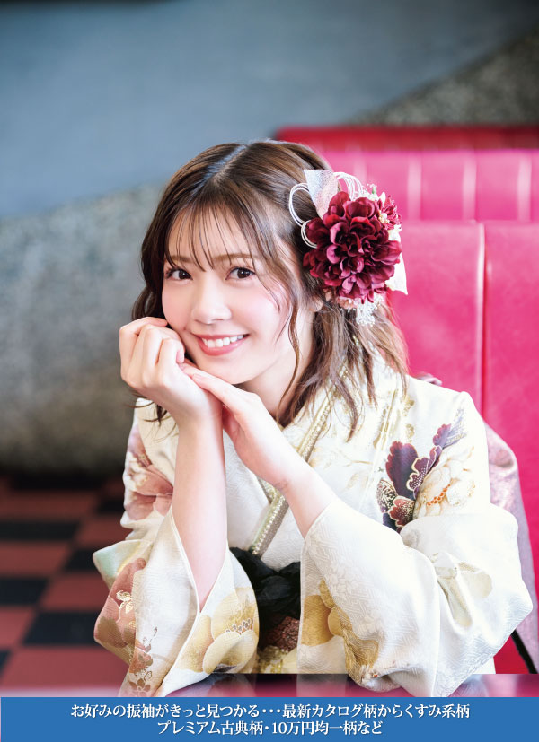 赤と白の大きな花の髪飾りをつけた花柄の着物姿の若い女性が、赤いベンチに座り、両手にあごを乗せて微笑んでいる。画像下部の青いバナーには日本語のテキストが表示されている。.