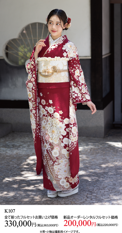伝統的な赤と白の花柄の着物を着た若い女性が、屋外の石畳の道に立ち、優しく微笑んでいる。画像の下に日本語のテキストと価格が表示されている。.